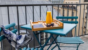 En balkon med et bord dækket til morgenmad, inklusive en bakke med et glas vand, et glas appelsinjuice og solbriller.