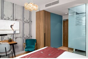 Una moderna camera d'hotel con un letto, una poltrona color petrolio, un pannello di legno a parete e una grande finestra.