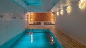 En moderne indendørs swimmingpool med træbænk og vægmonteret lys.