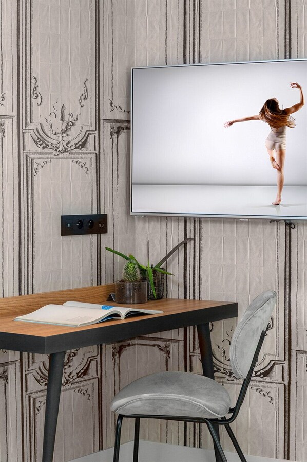 Une pièce comprenant une table en bois, une chaise, une plante en pot et un téléviseur diffusant une représentation de danse classique.