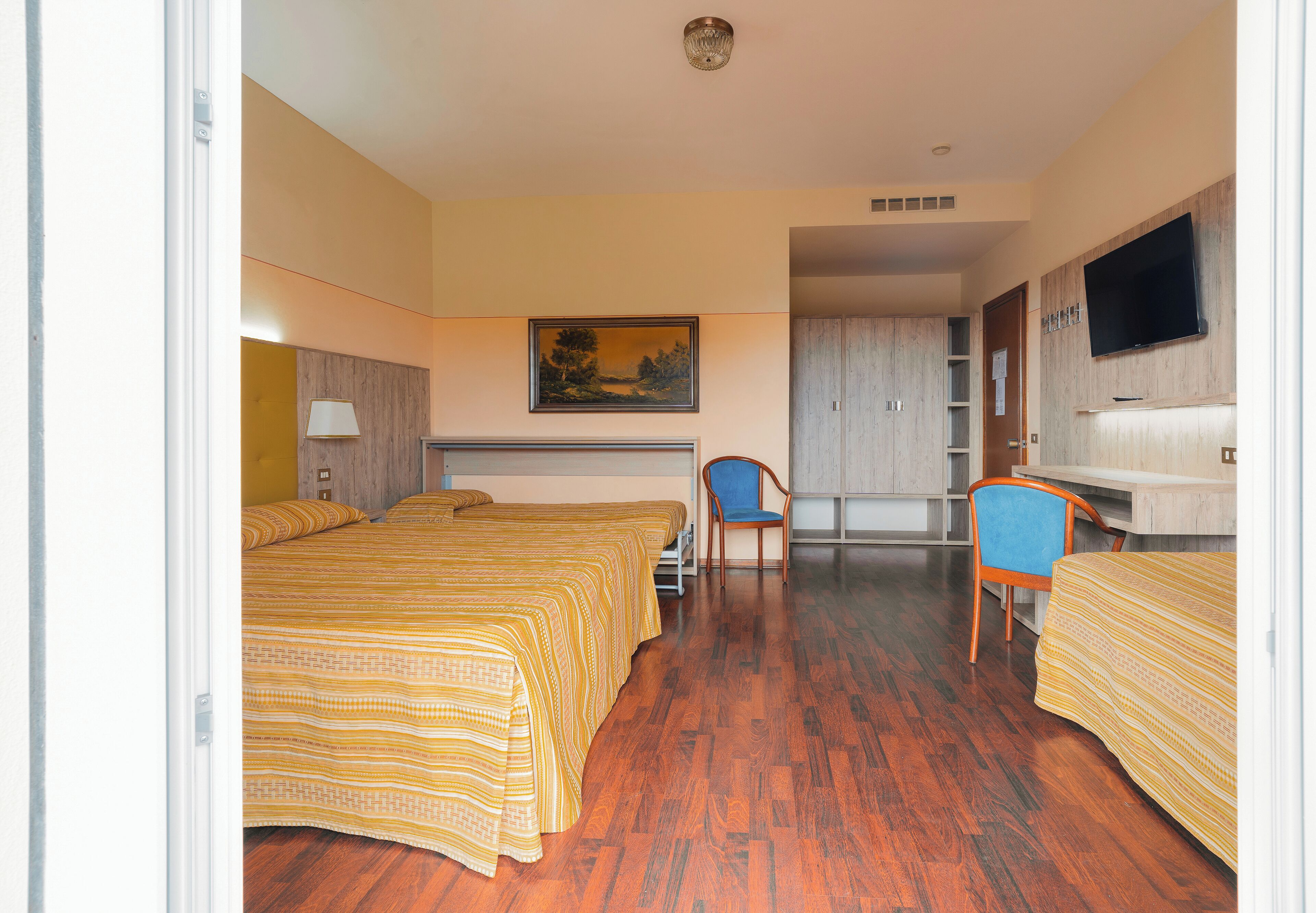 A hotel room with two beds, a desk, a chair, a TV, and a painting on the wall.