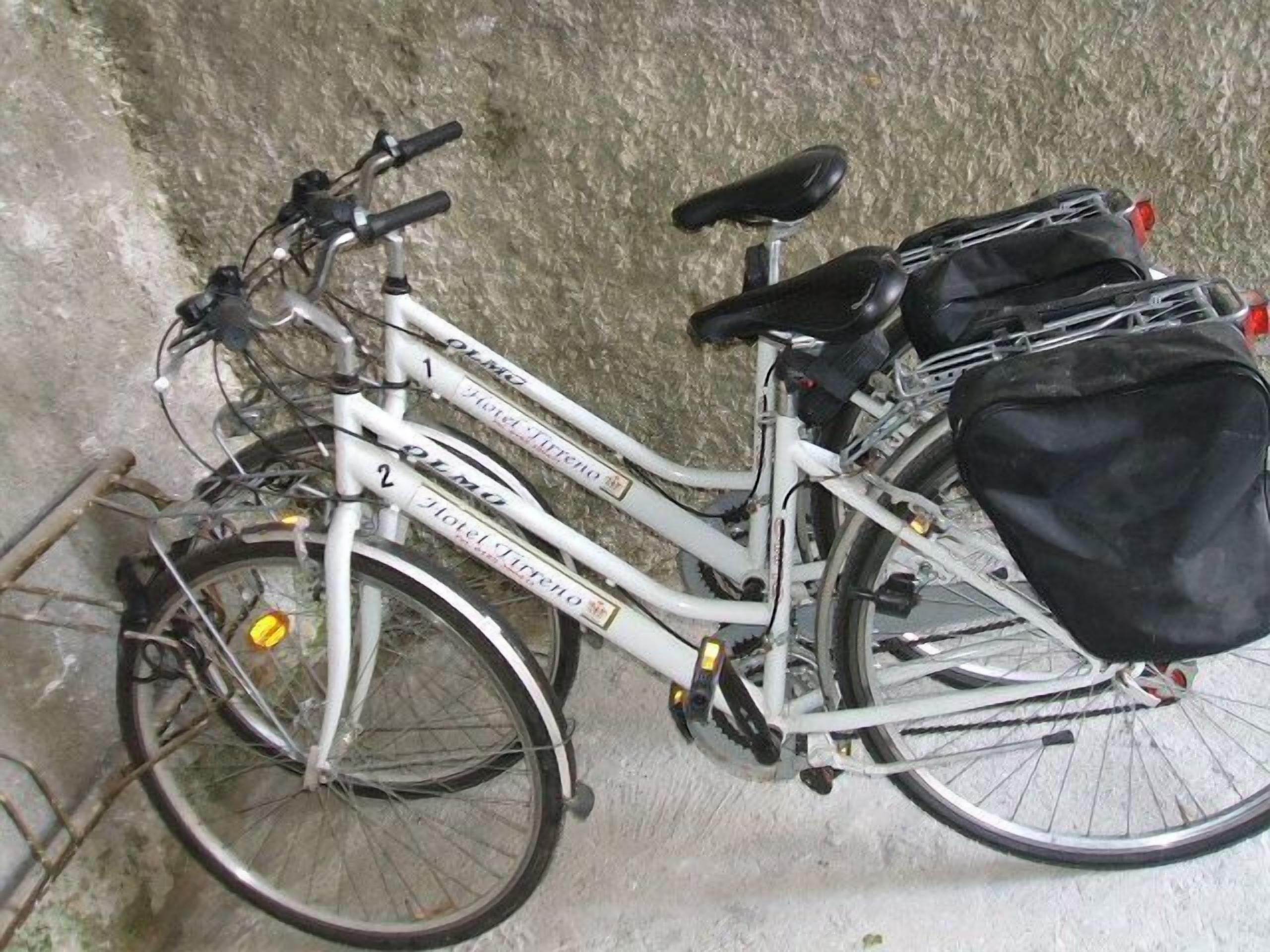 En vit cykel med en svart väska fastsatt på pakethållaren bak, lutad mot en vägg med en tydlig yta.