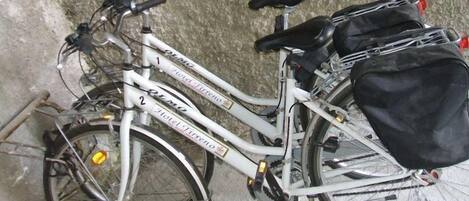 Una bicicleta blanca con una bolsa negra sujeta al portaequipajes trasero, apoyada contra una pared con textura.