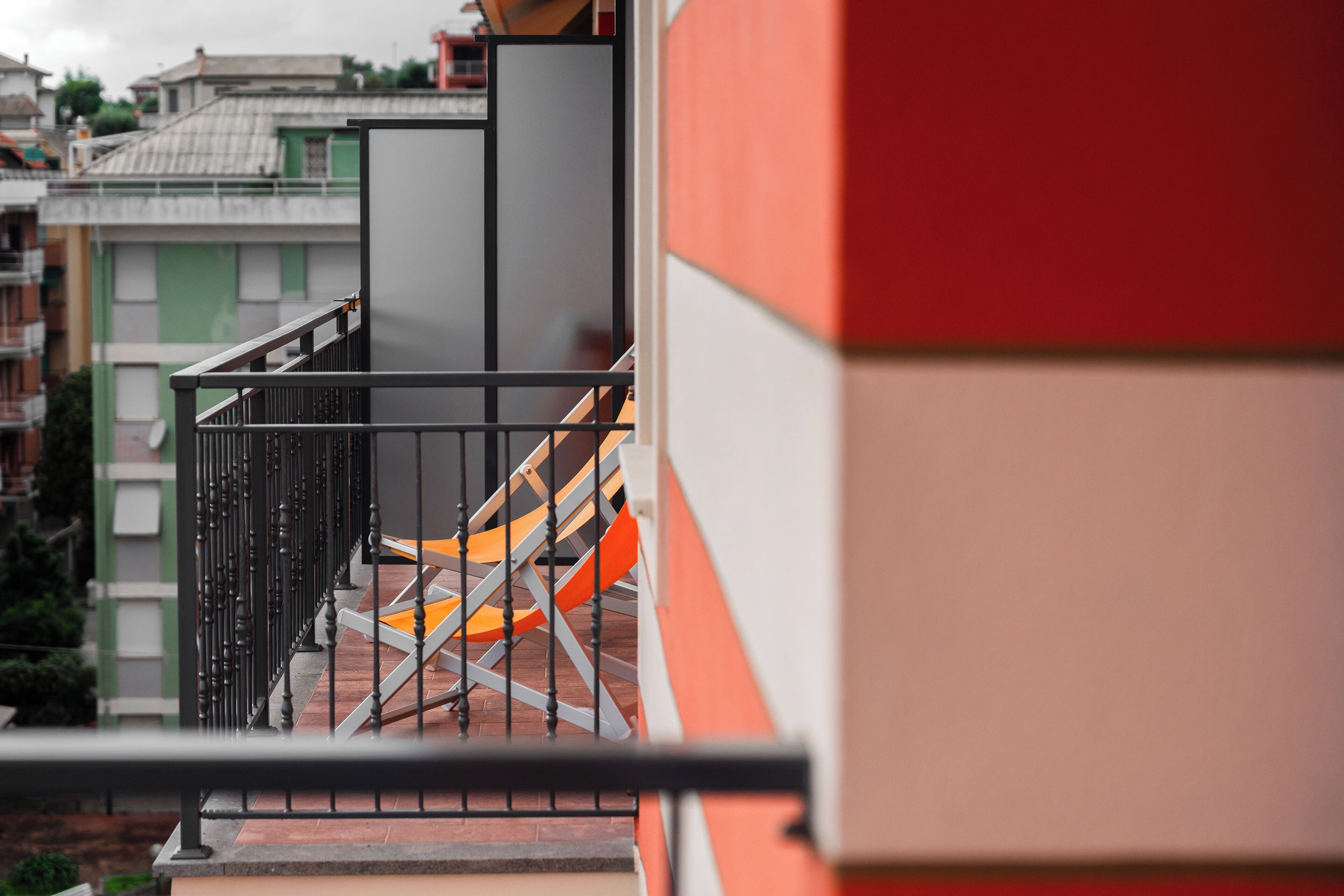 Un balcone con ringhiera metallica, una sedia e una vista parziale di un edificio.
