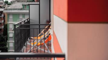 Un balcone con ringhiera metallica, una sedia e una vista parziale di un edificio.