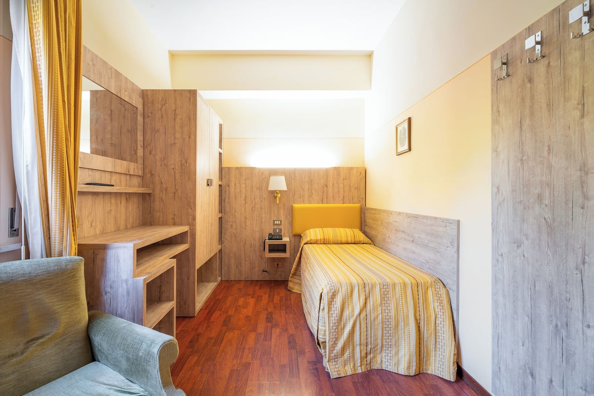 Une chambre d’hôtel de taille réduite, comprenant un lit, un bureau, une chaise et une armoire.