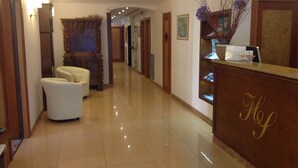Zona de recepción de un hotel con suelo pulido, un mostrador de recepción y un área de asientos con dos sillones.