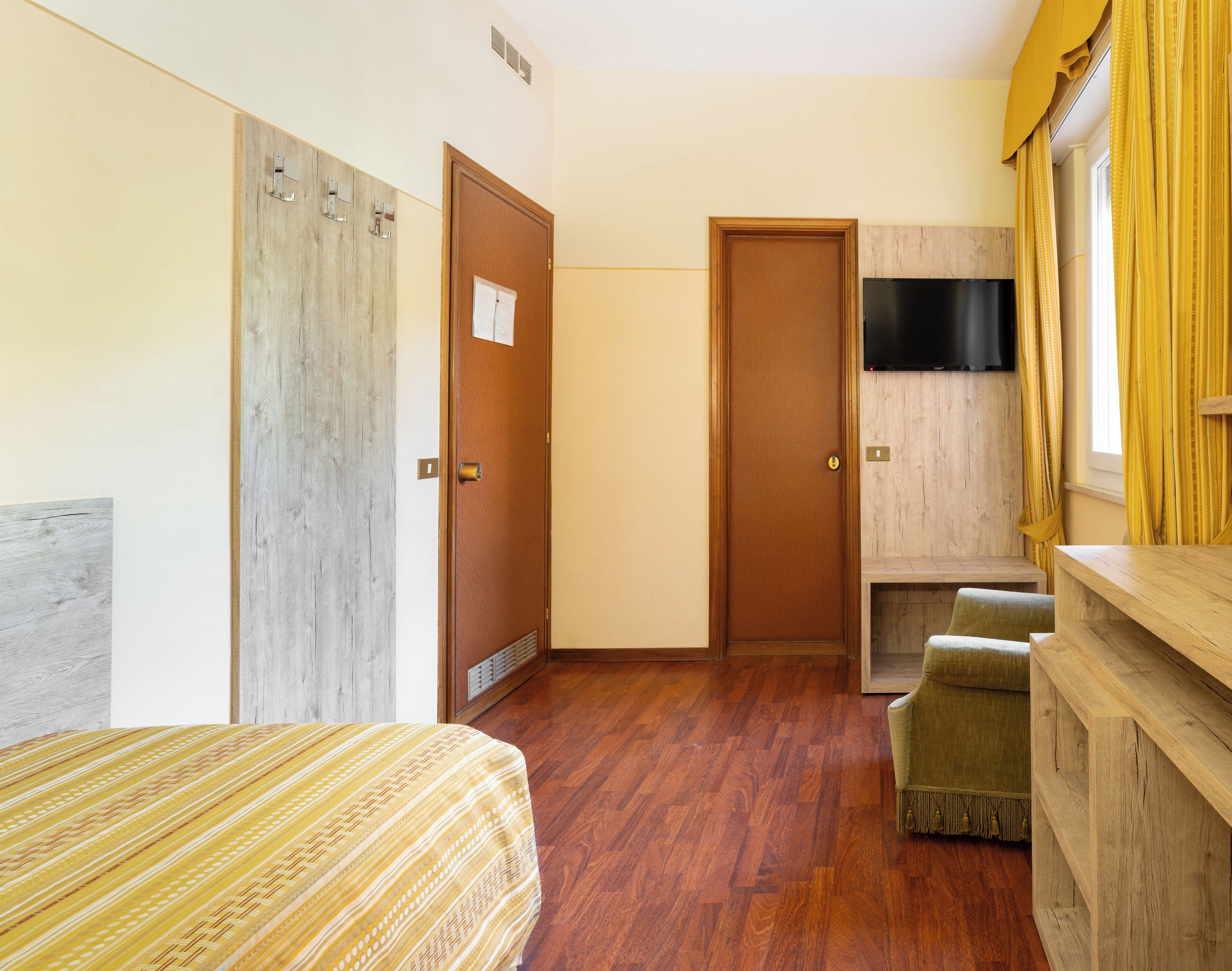Ein Hotelzimmer mit Bett, Holzschrank, Fernseher und einer kleinen Sitzecke.