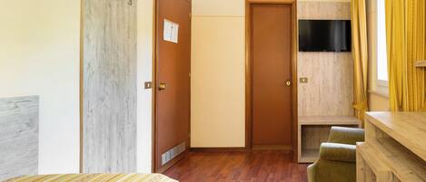Ein Hotelzimmer mit Bett, Holzschrank, Fernseher und einer kleinen Sitzecke.