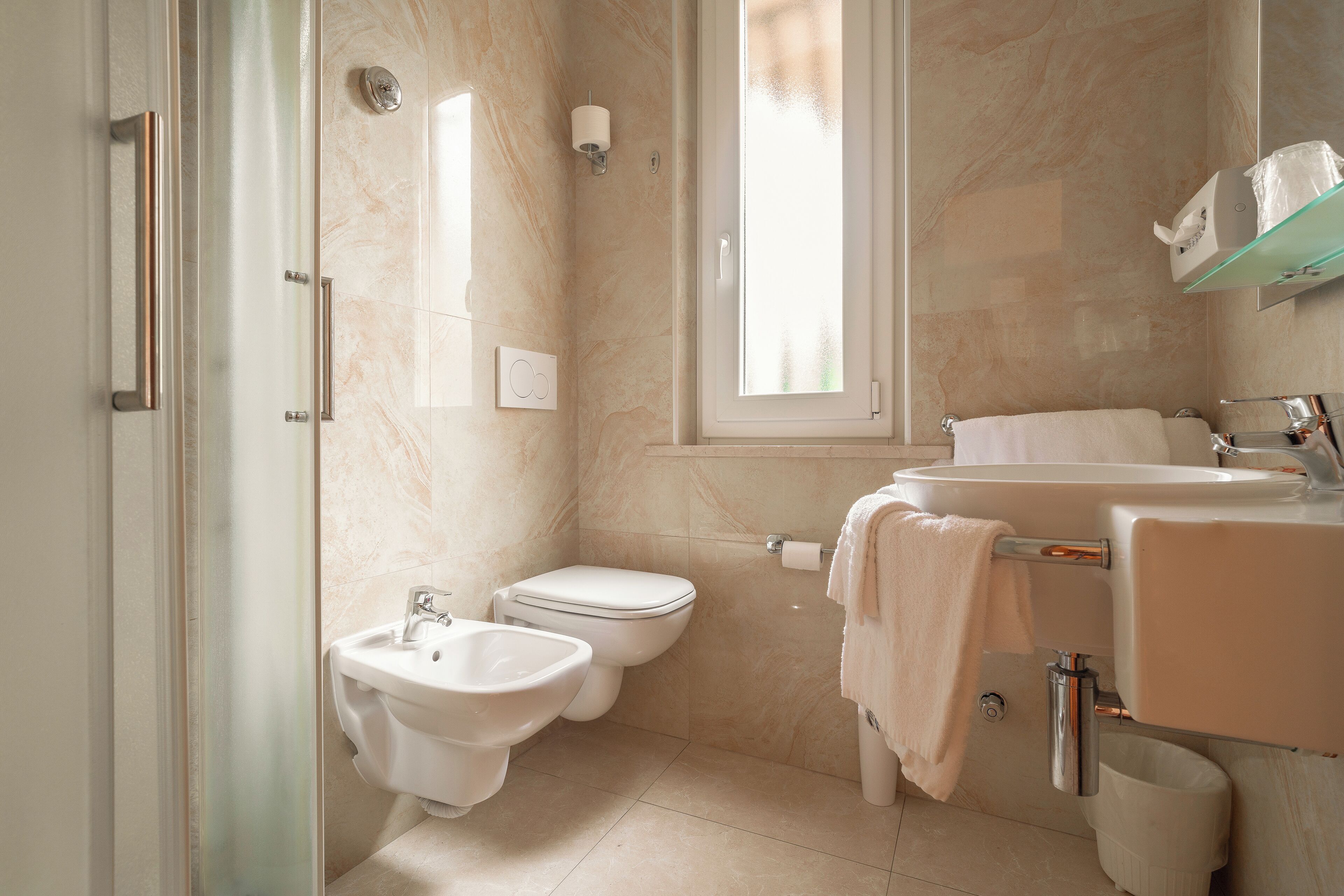 Une salle de bain moderne équipée d’un bidet, de toilettes, d’un lavabo et d’une douche à parois en verre.