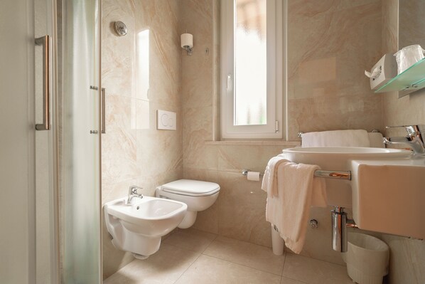 A modern bathroom with a bidet, toilet, sink, and glass shower enclosure.