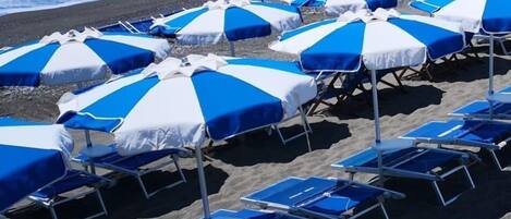 A beach with rows of blue and white striped beach umbrellas and lounge chairs.