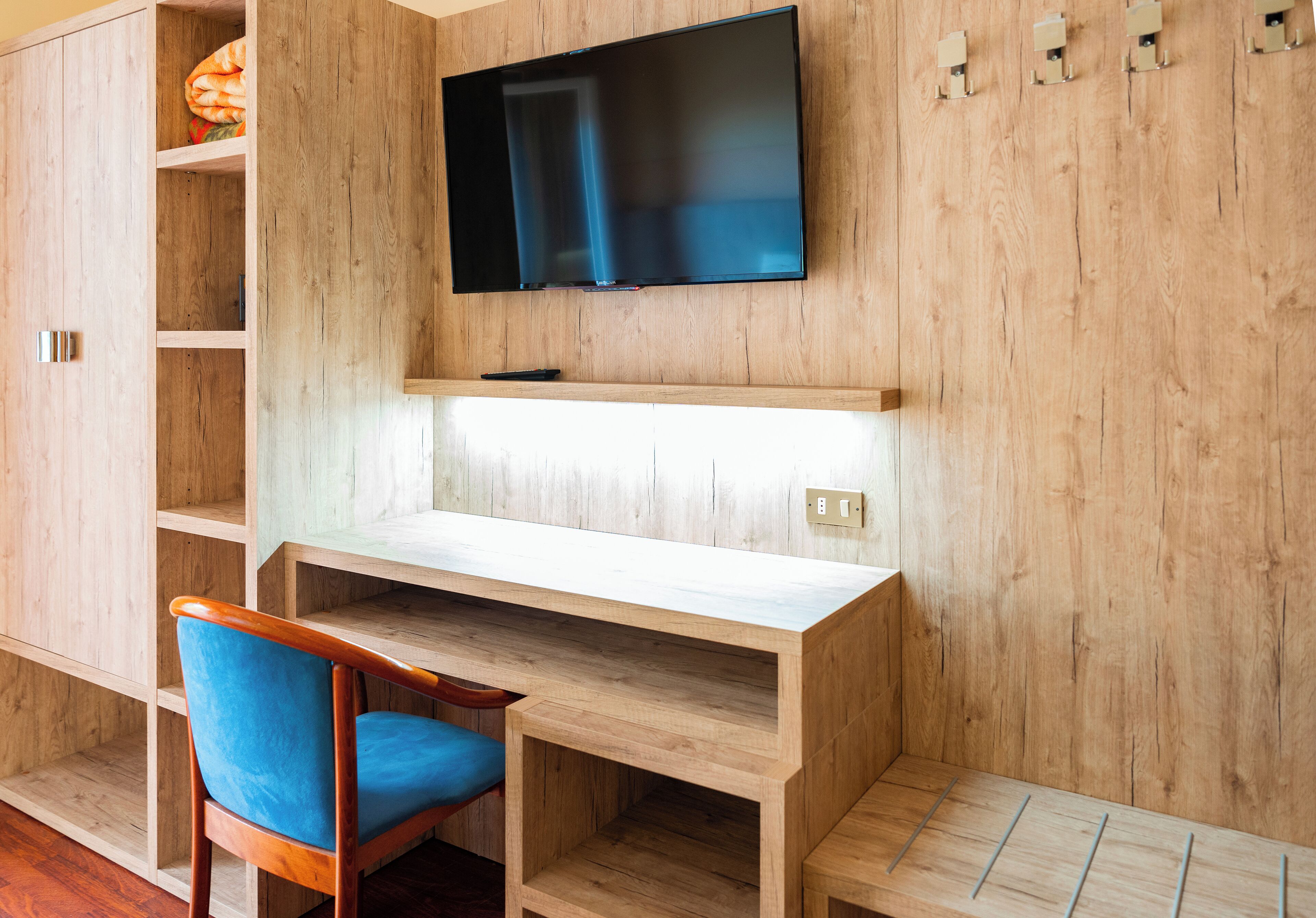 A wooden room with a TV mounted on the wall, a desk, and a chair.