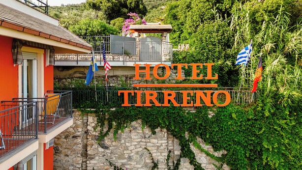 Un hotel llamado "HOTEL TIRRENIO" con paredes de piedra, un balcón y banderas.