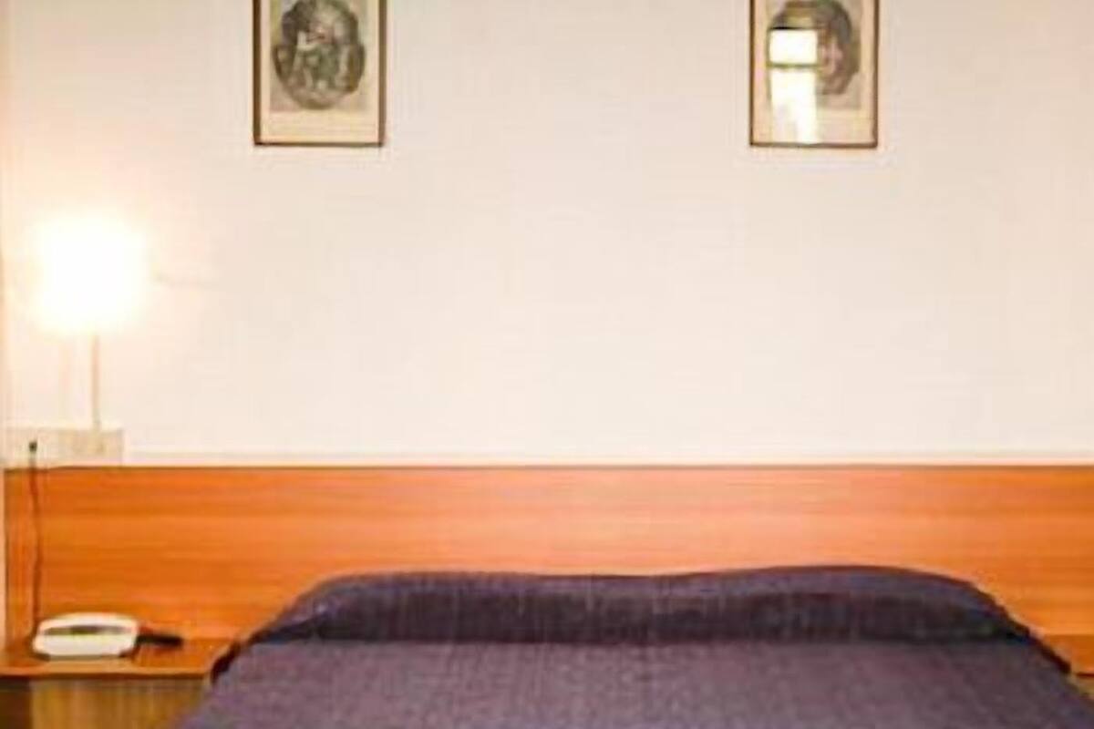 A room with a wooden headboard, a single bed with a blue bedspread, a bedside table with a lamp, and two framed pictures on the wall.