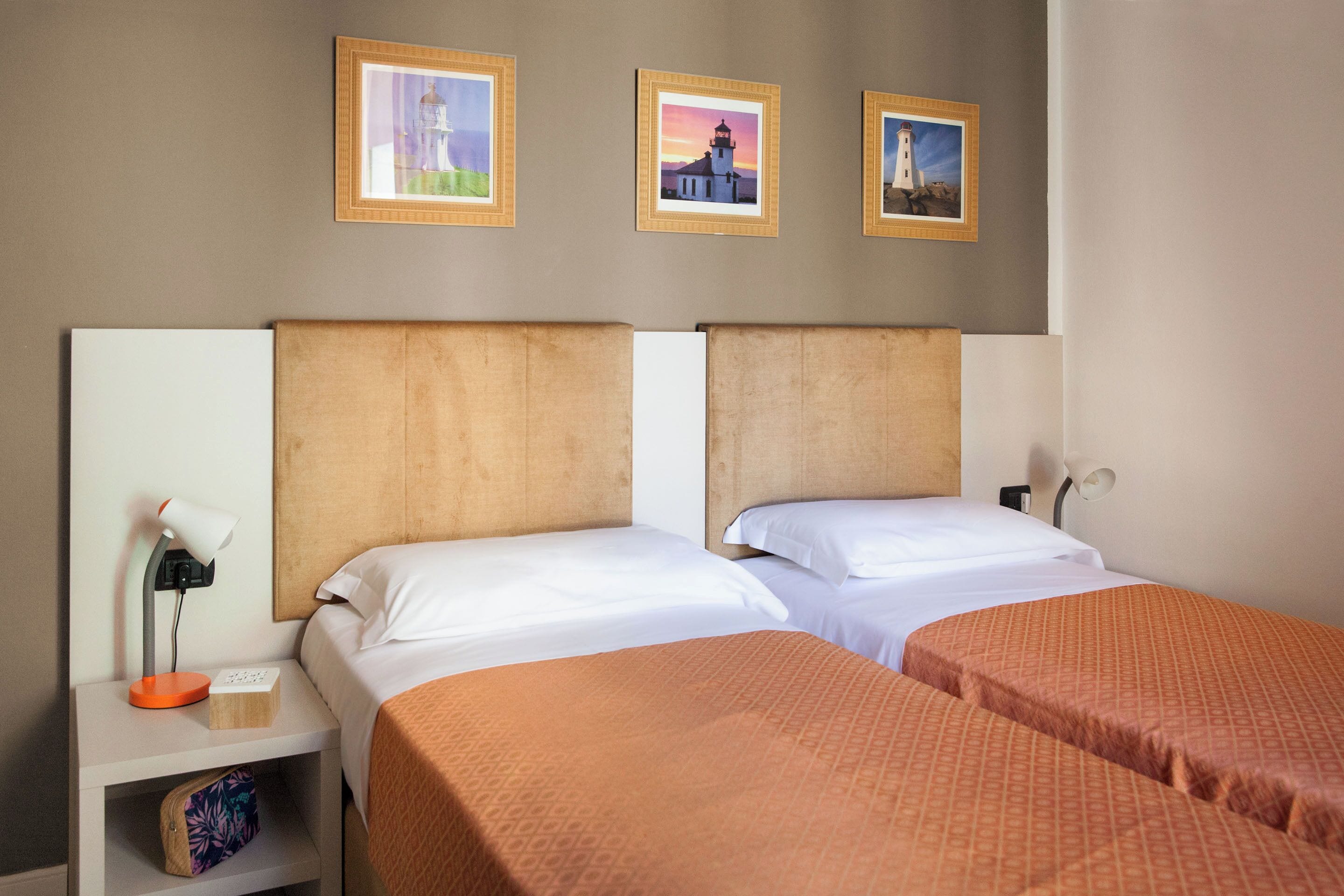 A hotel room with two beds, a nightstand with a lamp, and three framed pictures on the wall.