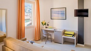 Una habitación de hotel moderna con sofá, escritorio, silla, televisor y ventana con cortinas.