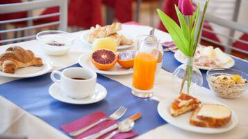 Una mesa de desayuno con platos de comida, un vaso de jugo de naranja, una taza de café y un florero con una flor.