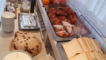 Un bufé con diversos alimentos, entre ellos pan, pasteles y frutas.