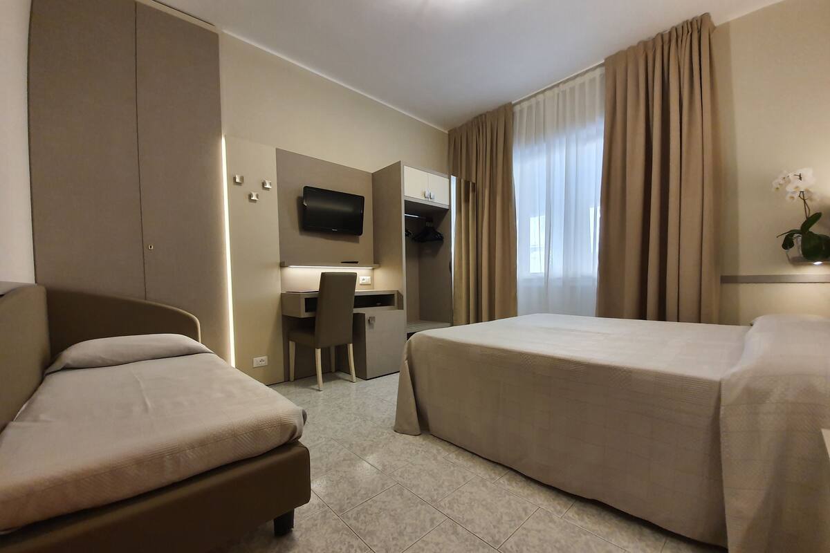Een hotelkamer met twee bedden, een bureau, een stoel, een televisie en een plant.