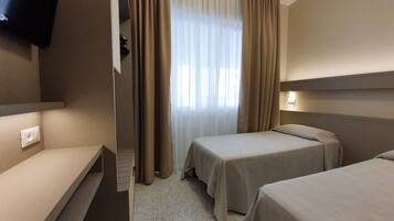 A hotel room with two single beds, a TV mounted on the wall, and a window with curtains.