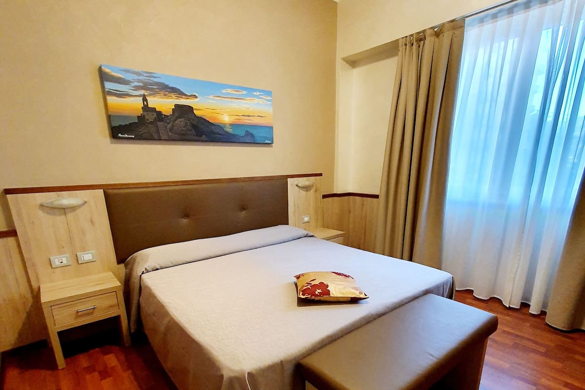 Een hotelkamer met een bed, nachtkastje, bankje en een schilderij aan de muur.
