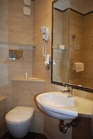 Baño con inodoro, lavamanos, secador de pelo y estante de vidrio.