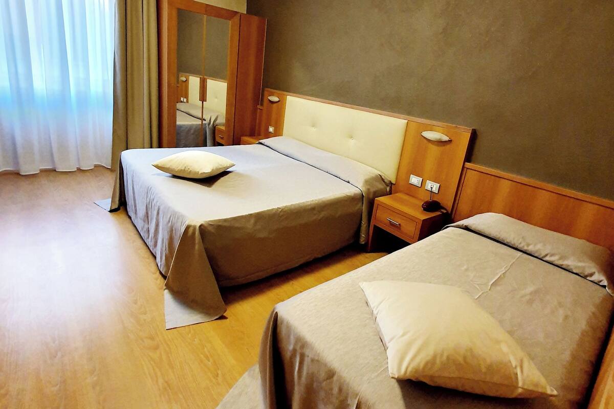 Hotelkamer met twee bedden, houten vloer, een grote spiegel en een raam met gordijnen.