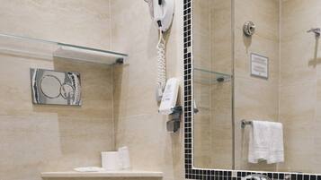 Casa de banho com sanita, lavatório, prateleira de vidro com produtos de higiene, secador de cabelo e espelho.