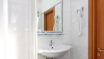 A bathroom with a white sink, a mirror, a hairdryer, and a blue trash bin.