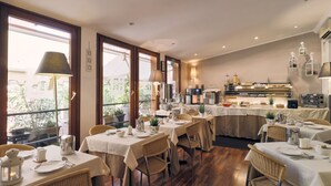 A restaurant with multiple tables set for dining, a kitchen area, and large windows allowing natural light. - Hotel Roberta (Mestre)