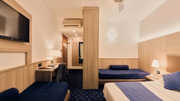 Habitación de hotel con dos camas individuales, un escritorio con silla, televisor de pantalla plana montado en la pared, lámpara y ventana.