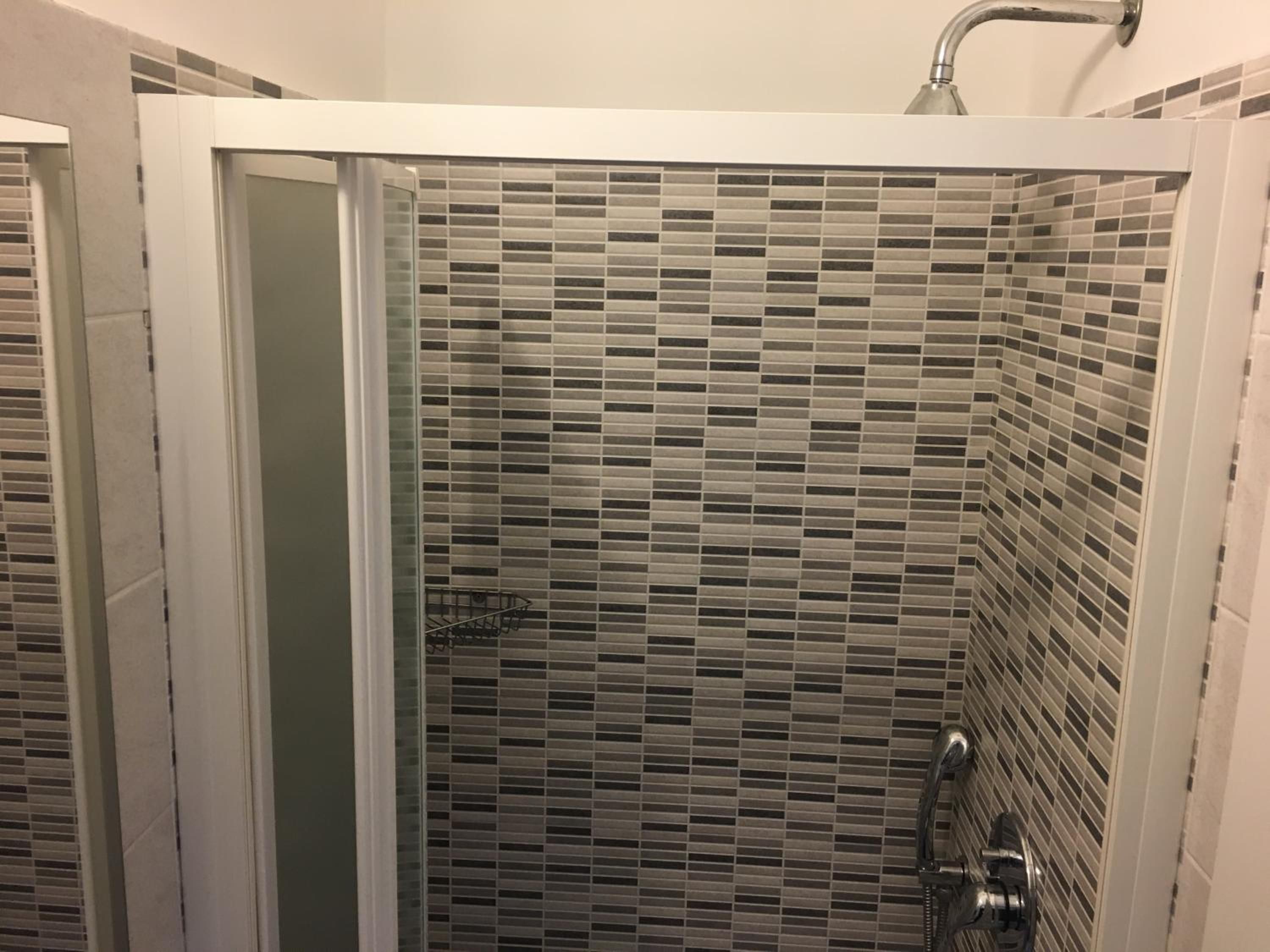 A shower with a tiled wall and a metal showerhead.