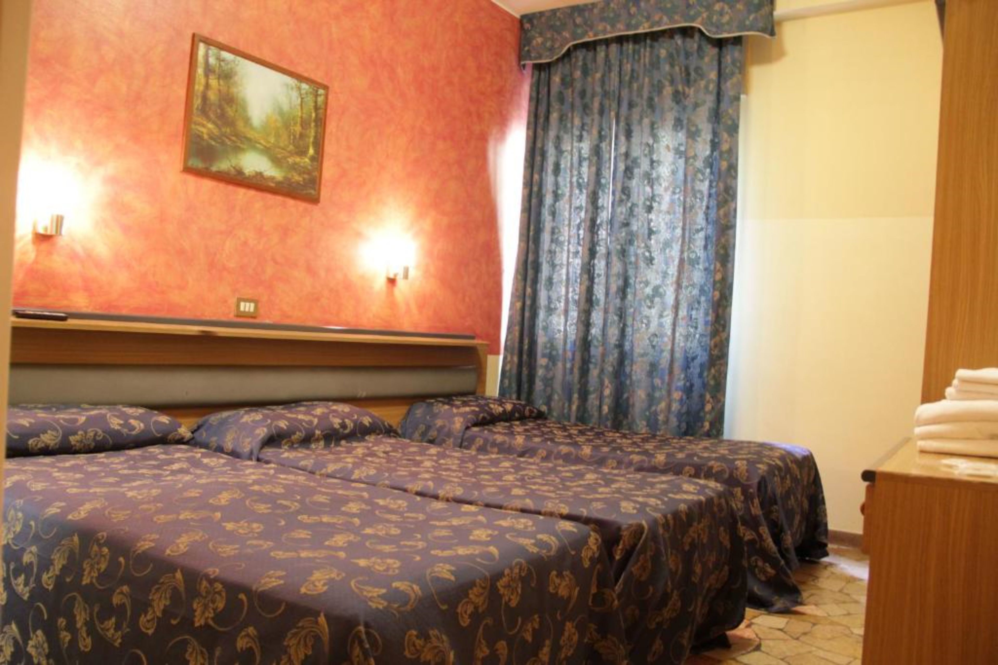 Une chambre d’hôtel avec deux lits, un tableau au mur et une fenêtre avec des rideaux.