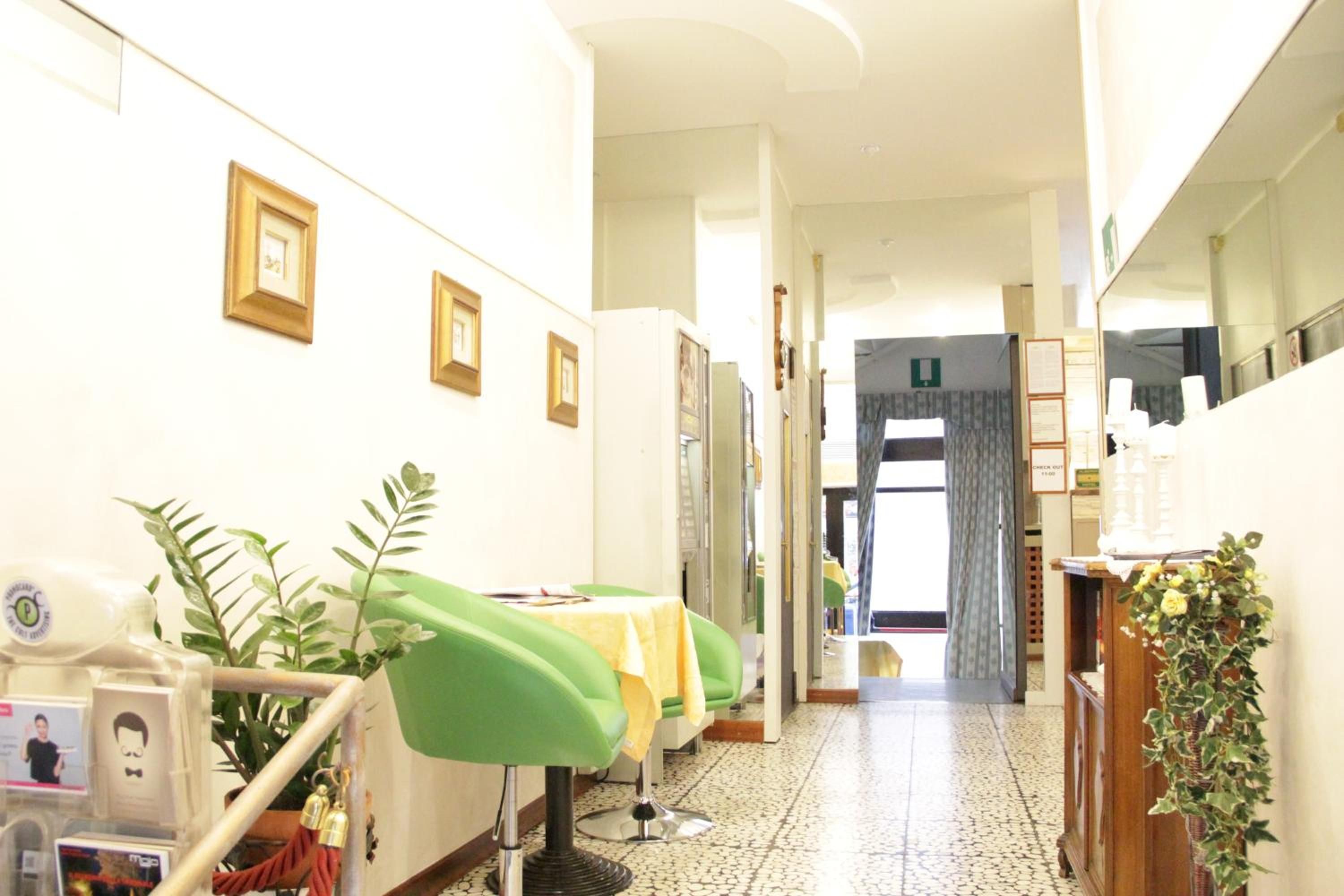A hallway with framed pictures on the wall, a green chair, a table with a yellow tablecloth, and a plant.