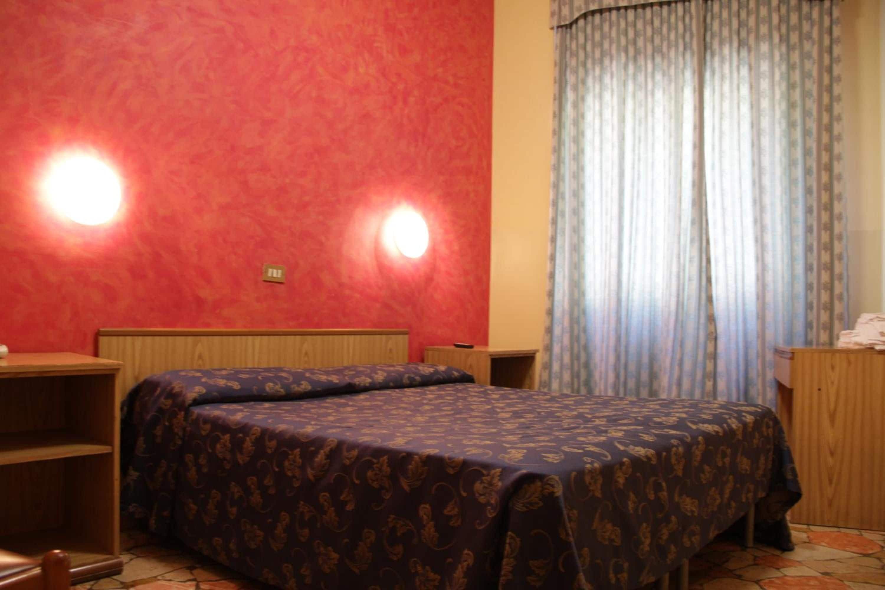 Una cama individual con una colcha estampada, cabecera de madera, mesita de noche y ventana con cortinas.