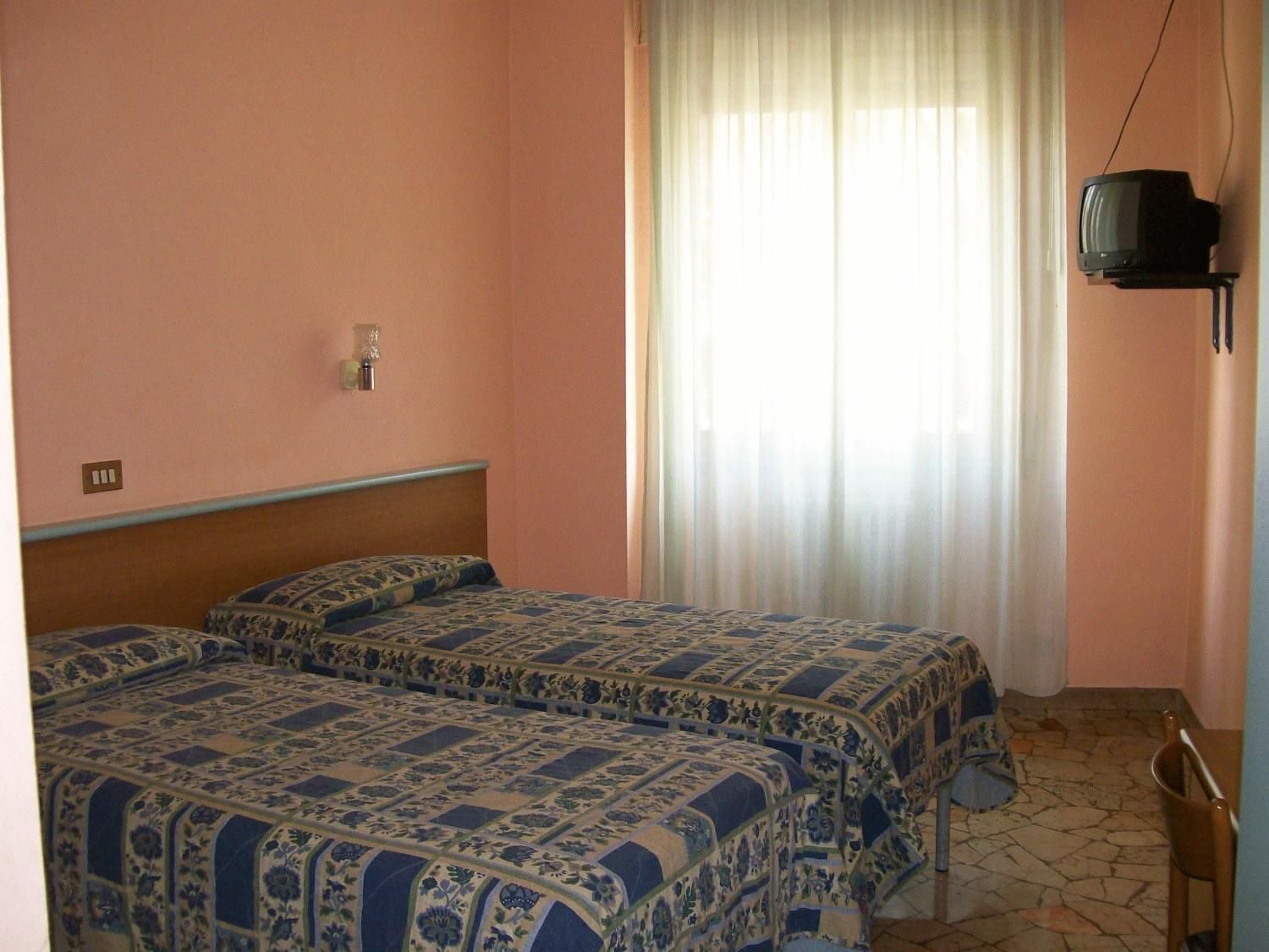 A bedroom with two beds, a television on a stand, and a window with curtains.