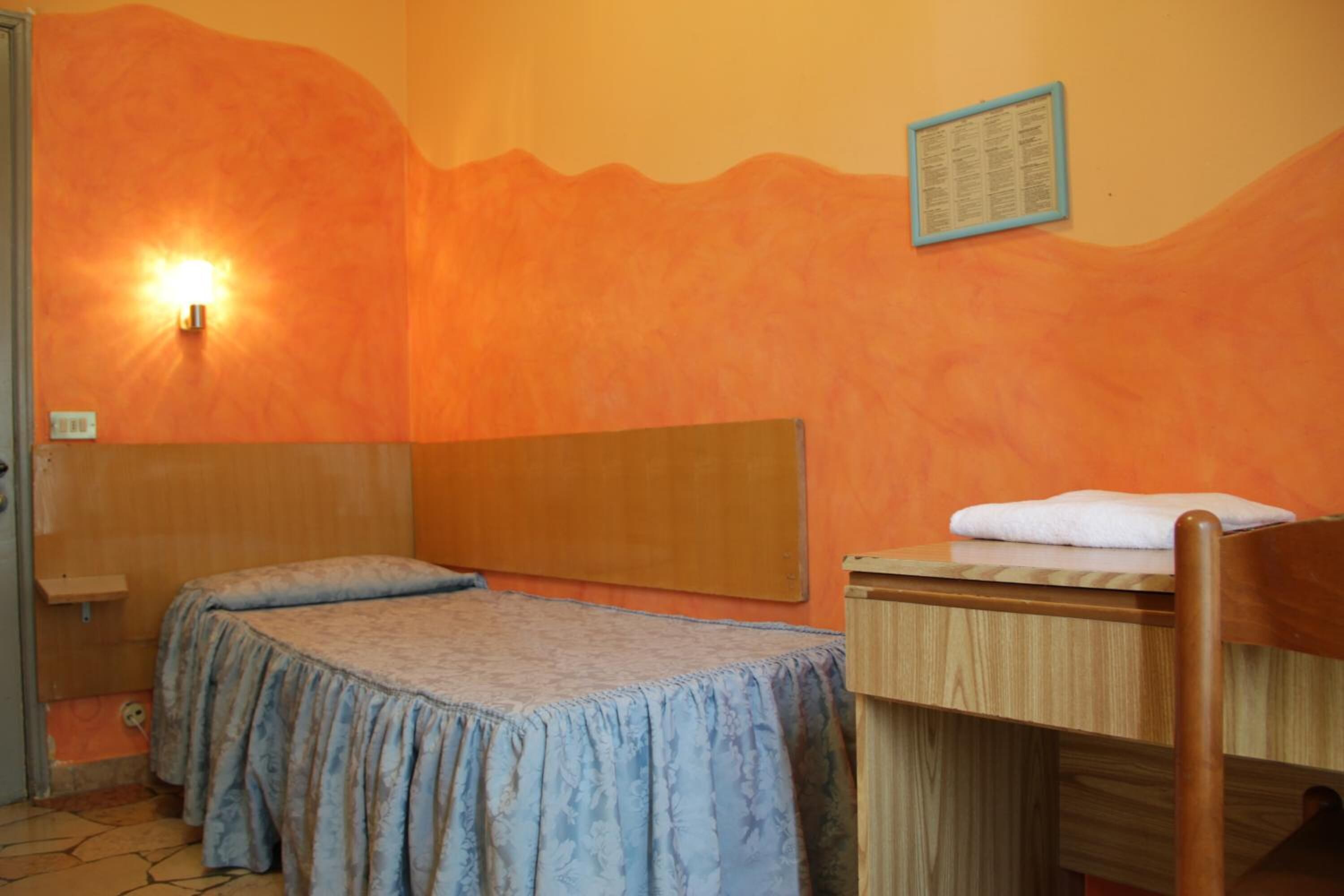 A room with two beds, a wooden desk, a wall-mounted light, and a framed menu on the wall.