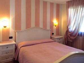 A bedroom with a bed, nightstands, and wall-mounted lamps. - Ernestina (Miane)