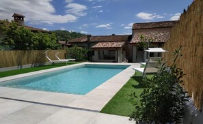 A rectangular swimming pool with a tiled deck, surrounded by a bamboo fence, and a grassy area. - Ernestina (Miane)