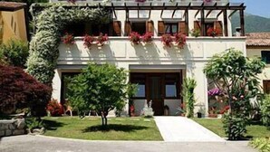 Un immeuble de deux étages doté d’un balcon, avec un jardin à l’avant et une montagne en arrière-plan.