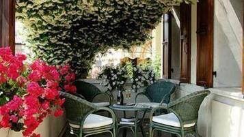 Um espaço de estar exterior estreito com mesa e cadeiras, rodeado por vegetação exuberante e flores vibrantes.