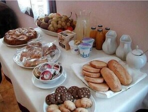 A table with various food items including bread, pastries, and a bowl of fruit. - Ernestina (Miane)