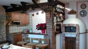 Une cuisine dotée d’un four en briques, de meubles en bois et d’un coin repas avec des chaises et une table dressée pour deux personnes.