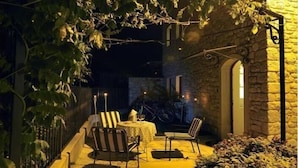 Un espace extérieur aménagé en patio, avec un mur en pierre, une table entourée de chaises et des guirlandes lumineuses.
