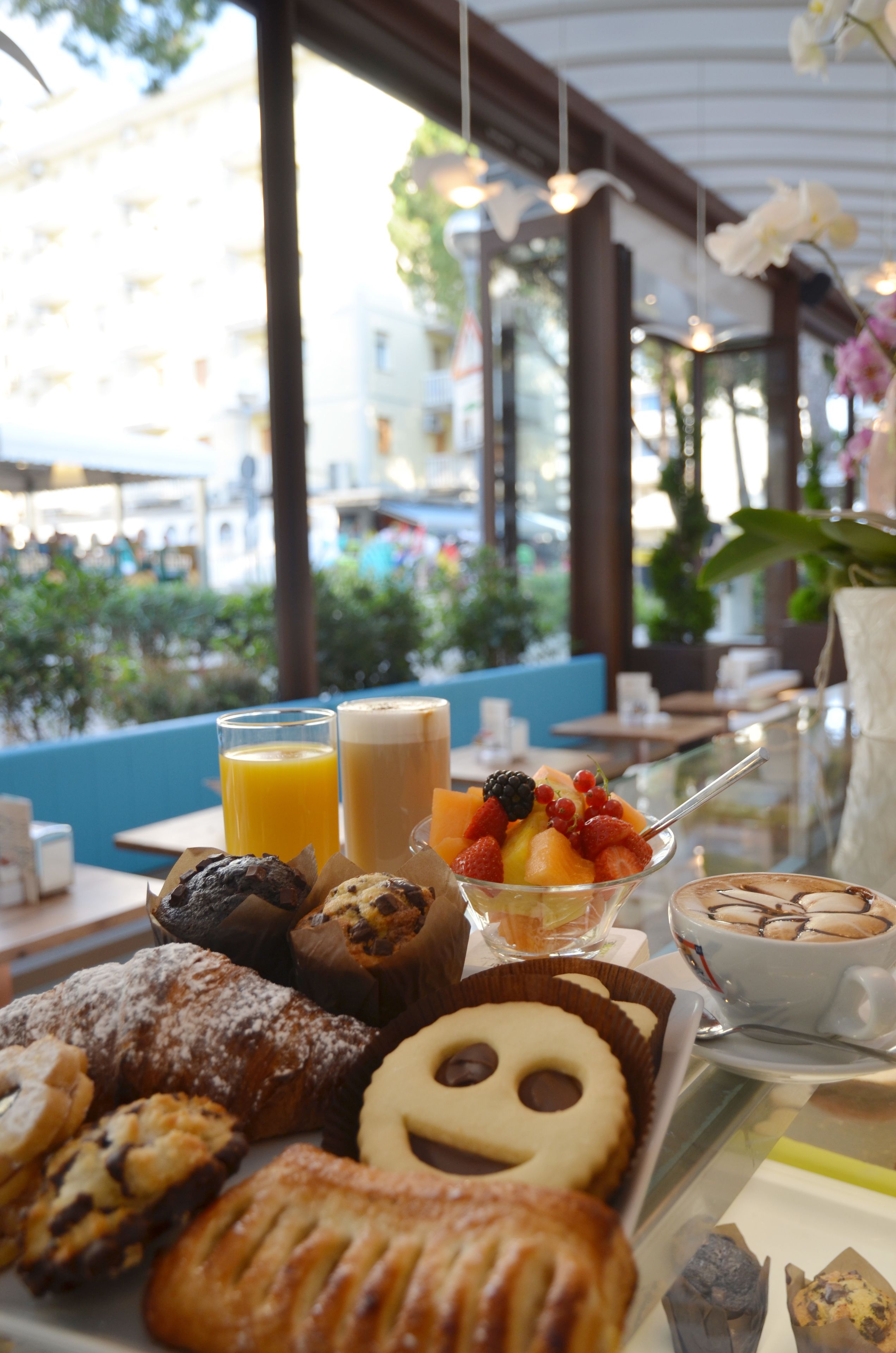 Buffet de café da manhã com pães, frutas e bebidas em uma mesa com vista para a cidade.