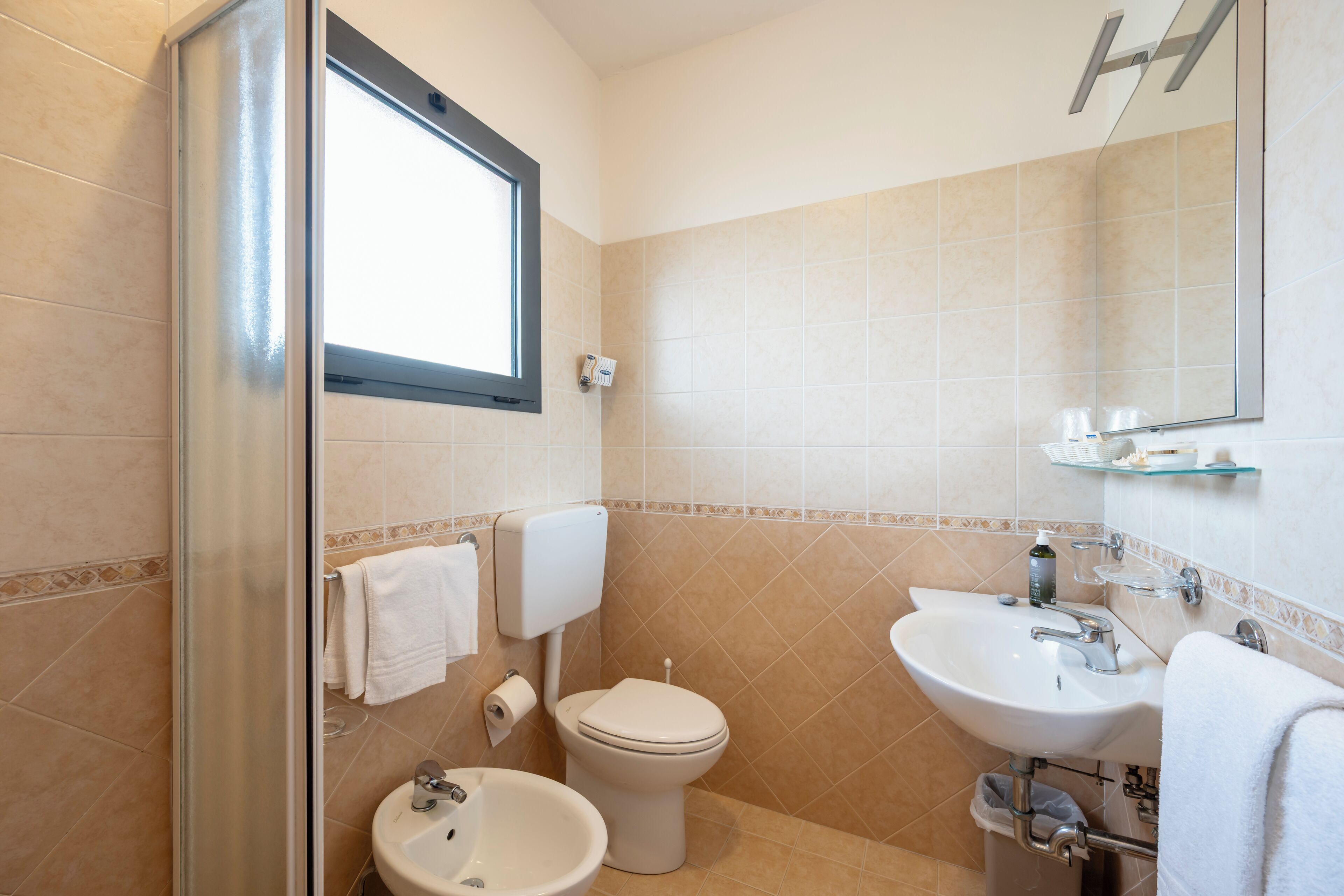 A bathroom with a toilet, bidet, sink, and a glass shower enclosure.