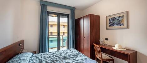 A hotel room with a bed, a desk, a chair, a wardrobe, and a balcony with curtains.