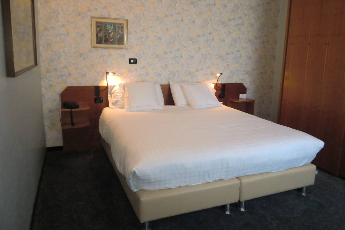 A neatly made bed with a white duvet and pillows, a bedside table with a lamp, and a framed picture on the wall.