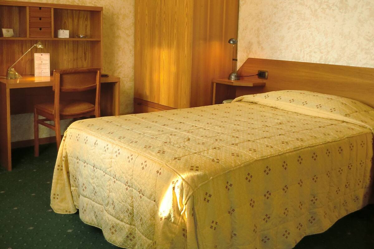 A room with a bed, a desk, a wardrobe, and a wall-mounted light fixture.